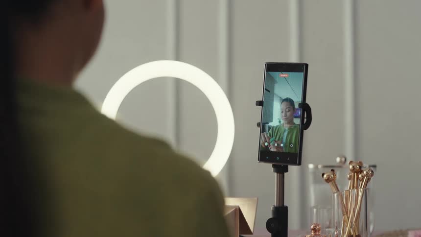 Woman records a video with a phone on a tripod and a ring light indoors