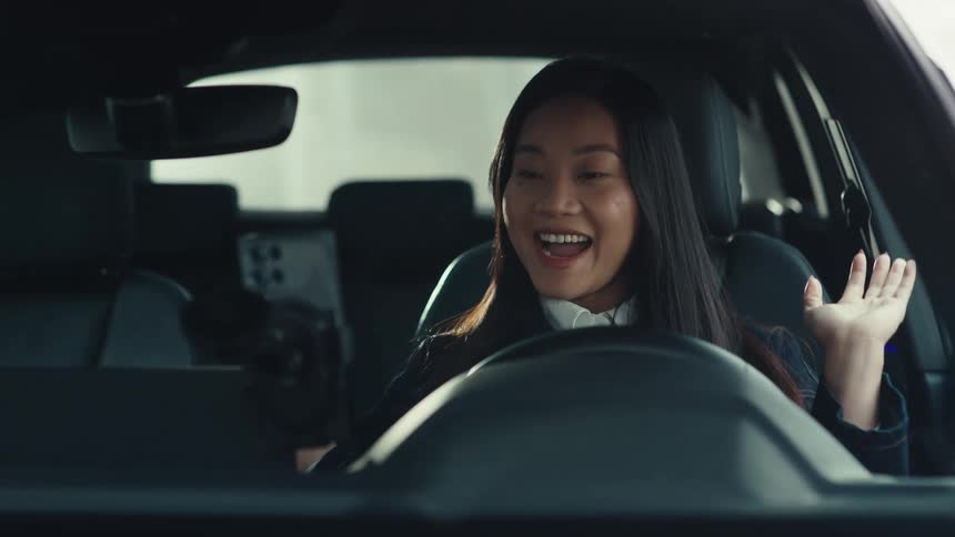 Woman adjusts cell phone on the dashboard and begins to speak with a smile
