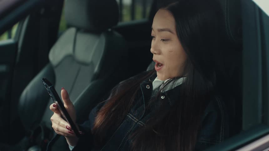 Woman smiles while sitting in a parked car and viewing her smartphone