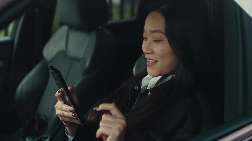 Woman sits in the drivers seat of an automobile holding her phone as she has a conversation