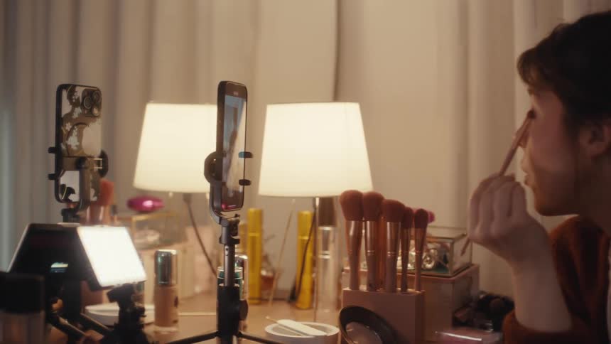 Woman uses a smartphone to record herself putting on makeup