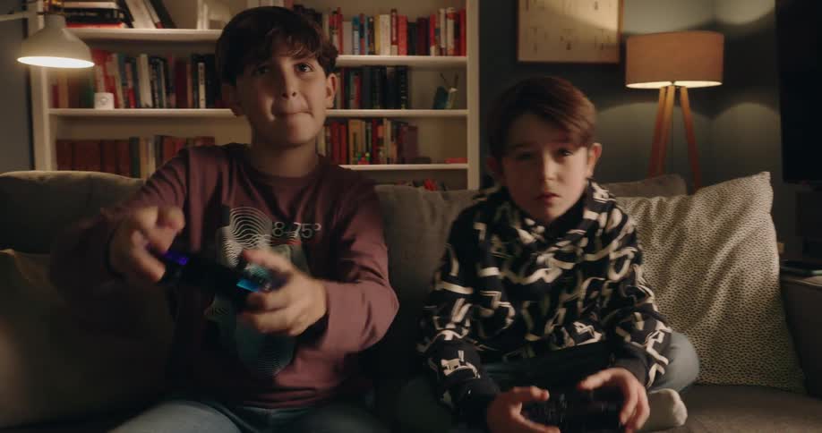 Two boys sitting on a couch play a video game with controllers in their hands