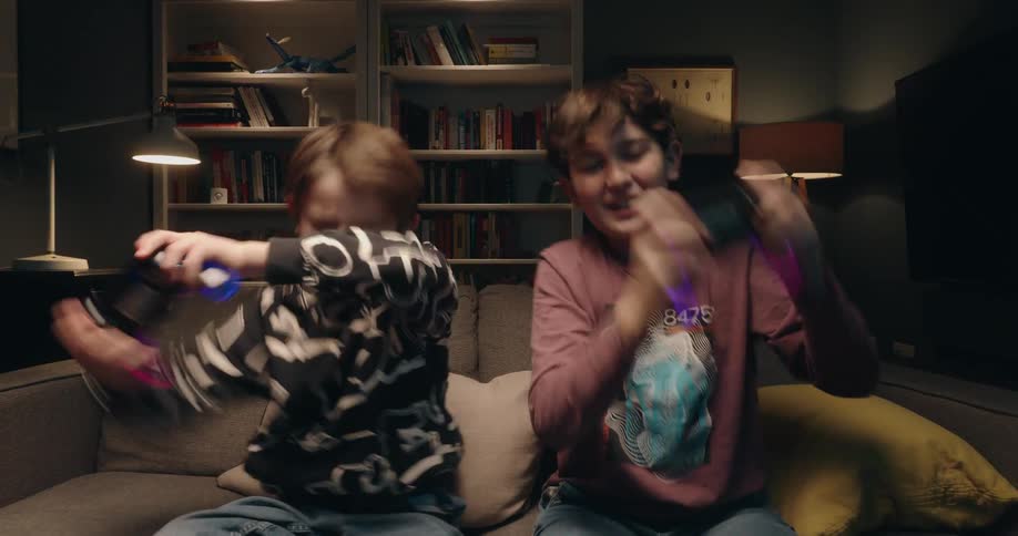 Two children sitting on a couch hold video game controllers in a living room
