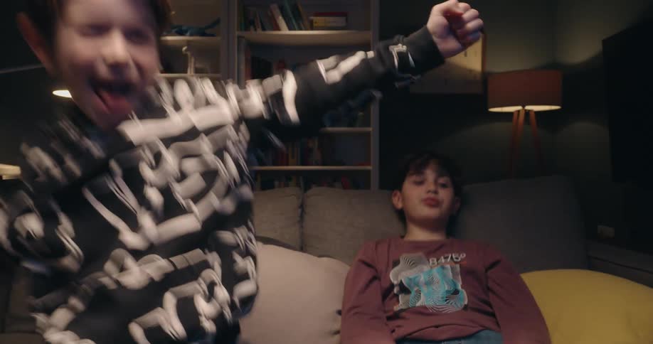 Two boys laughing and playing as they sit on the couch with video game controllers
