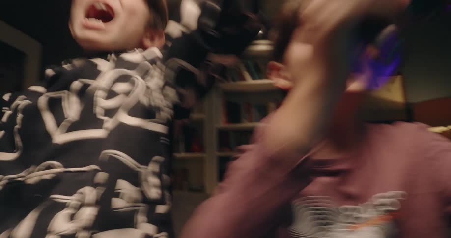 Two boys laughing and playing as they sit on the couch with video game controllers