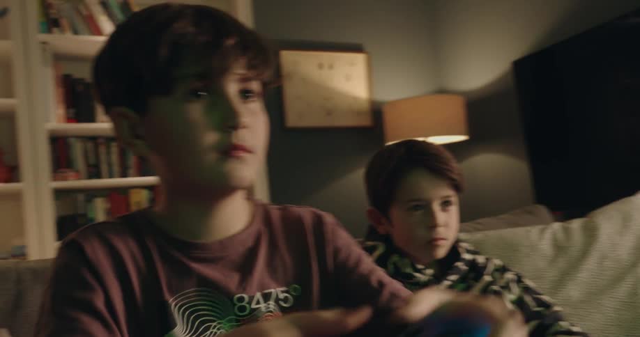 In the living room one boy frowns when losing in a video game while another boy smiles