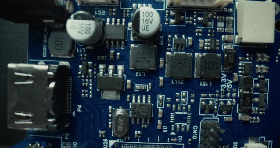 A topdown closeup shot pans across a blue printed circuit board revealing various electronic components like capacitors resistors and microchips soldered onto the surface alongside integrated ports and connectors