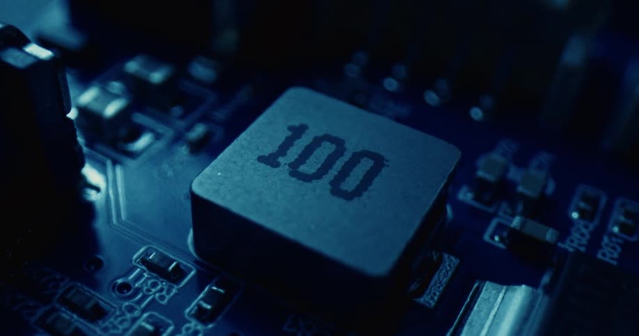 A square surfacemount inductor labeled 100 on a dark blue printed circuit boardthe camera pans slowly around the component highlighting the surrounding resistors capacitors and metallic solder joints under dim moody lighting
