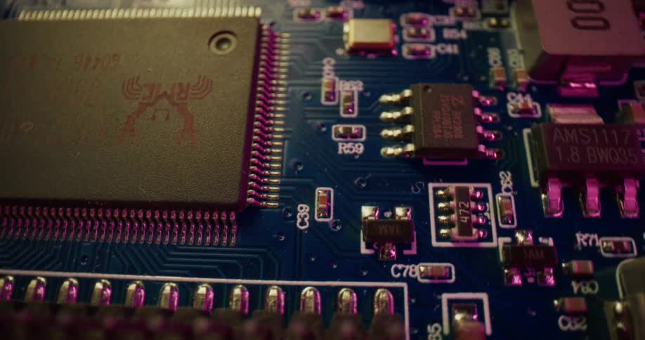 The camera pans across a detailed blue circuit board revealing various microchips resistors and electronic components illuminated by shifting pink and yellow lights
