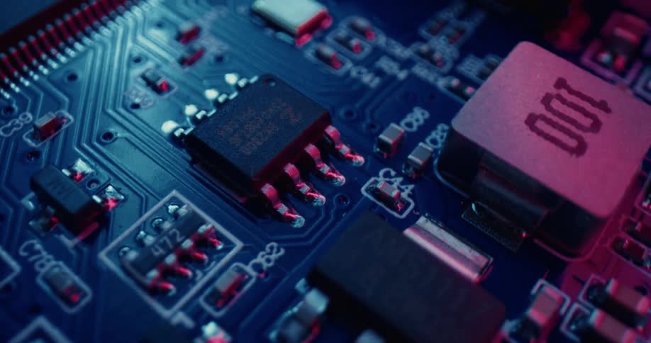 A closeup view shows a black circuit board under soft pink hued lighting