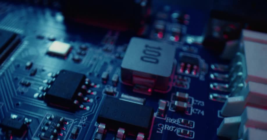 A closeup panning shot of a blue circuit board featuring various electronic components including microchips resistors and capacitors illuminated by blue and red light