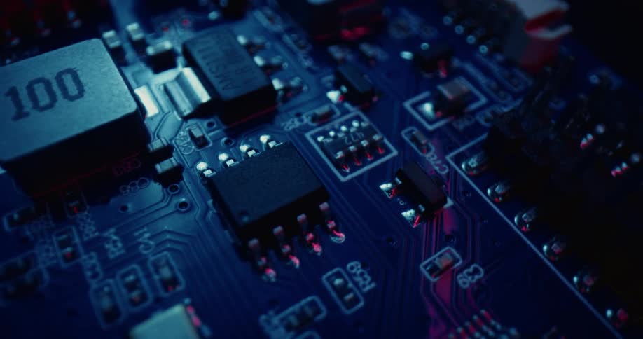 A closeup panning shot of a blue circuit board featuring various electronic components including microchips resistors and capacitors illuminated by blue and red light