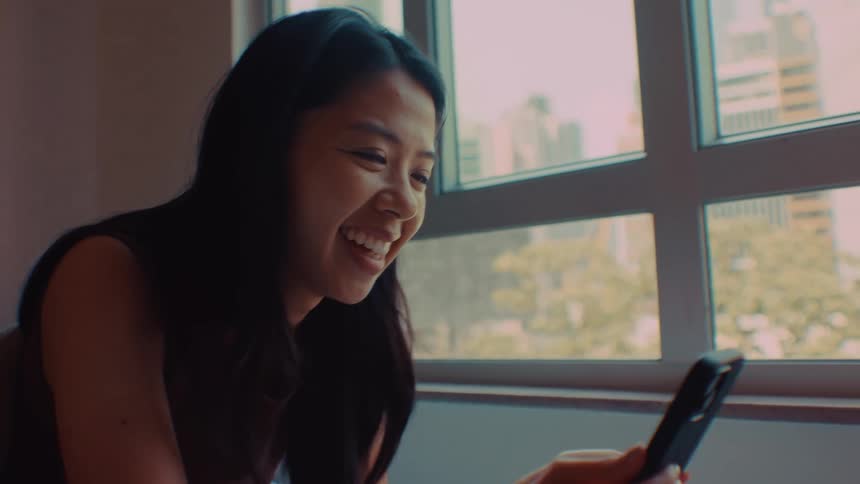 Teenage girl laughs as she sits holding her phone