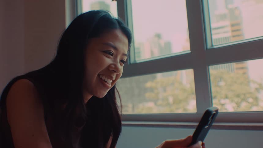 Teenage girl laughs as she sits holding her phone