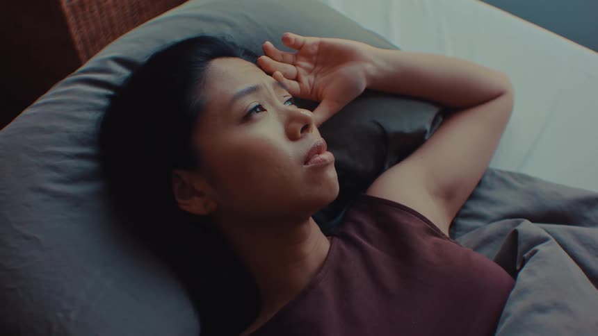 Woman lying on a bed rests her hand on her head while looking to the side