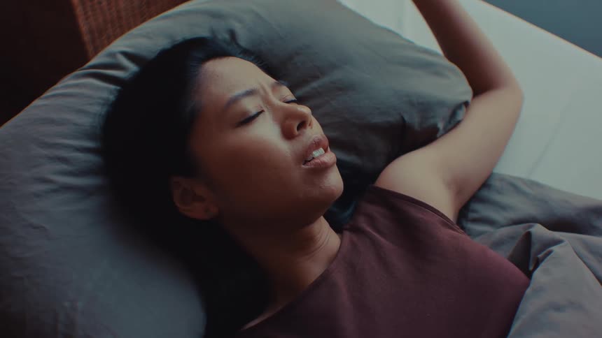 Woman lying on a bed rests her hand on her head while looking to the side