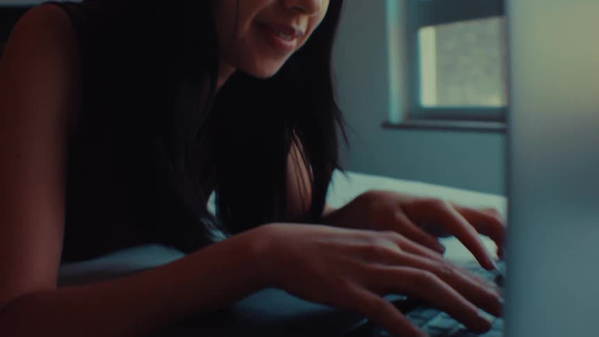 Woman smiles while lying on her bed and typing on a computer