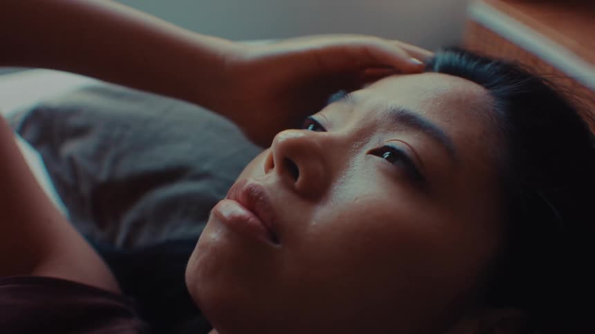 A woman weighed down by depression and stress lies on a bed in a softly lit bedroom