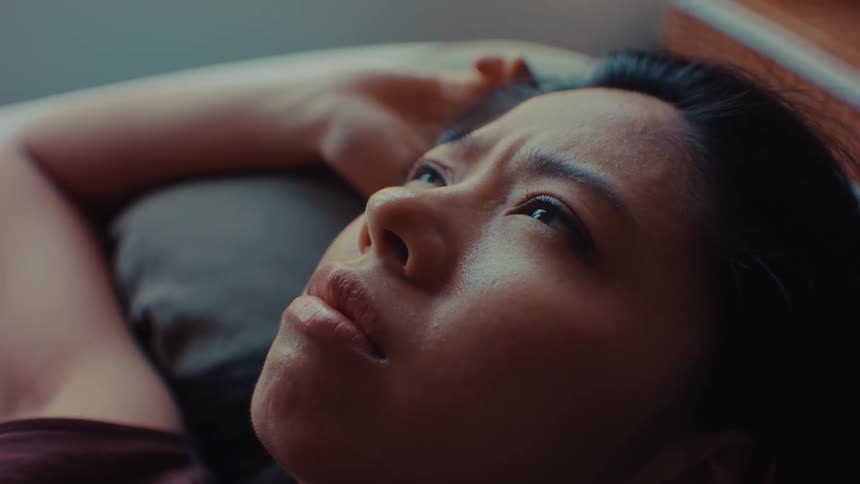 A woman weighed down by depression and stress lies on a bed in a softly lit bedroom