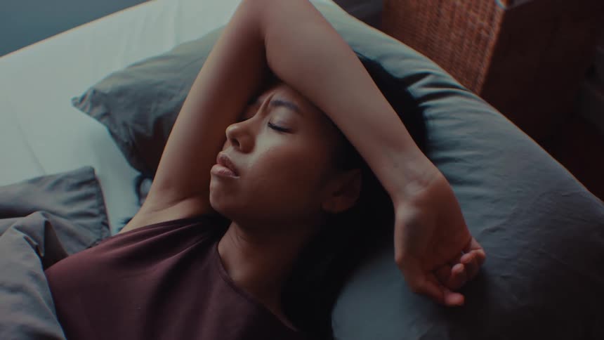 Woman lying on a bed keeps her arm resting above her head while looking to the side