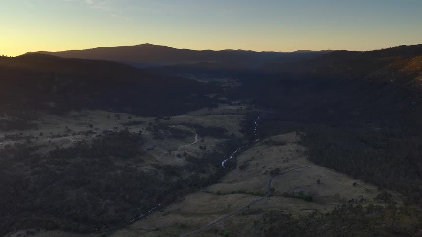 The sun is set behind a mountain range that near a hilly landscape