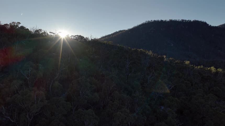 The sun shines brightly above some hills and mountains