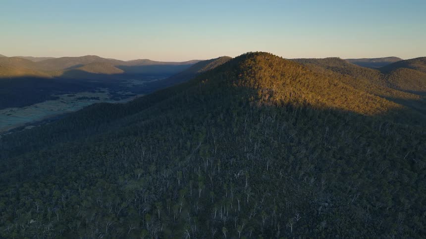Aerial view of forested mountains at dusk with sunlight casting long shadows across the landscape