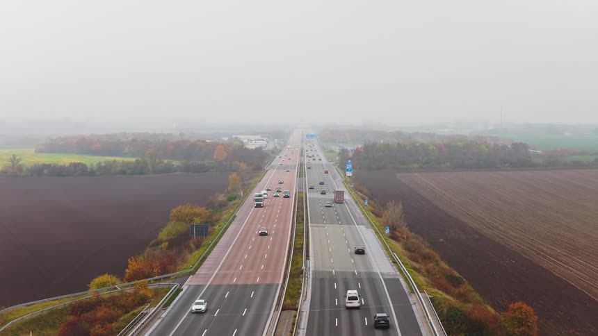 Traffic moving along a highway through rural autumn fields on a misty day