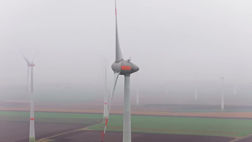 A windmill farm with several windmills under a foggy sky