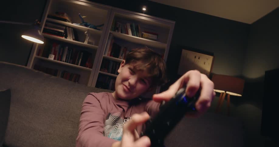A boy excitedly plays a video game while sitting on a couch in a cozy living room