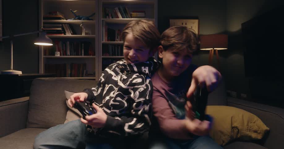 Children play video game on couch with lit bookshelf in background