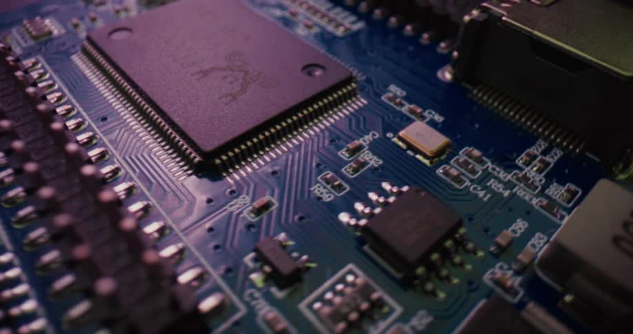 A camera pans across a blue circuit board illuminated by shifting red and blue lights that highlight the textures of microchips and soldered componentsthe closeup view reveals a dense landscape of electrical pathways pins and hardware creating a h