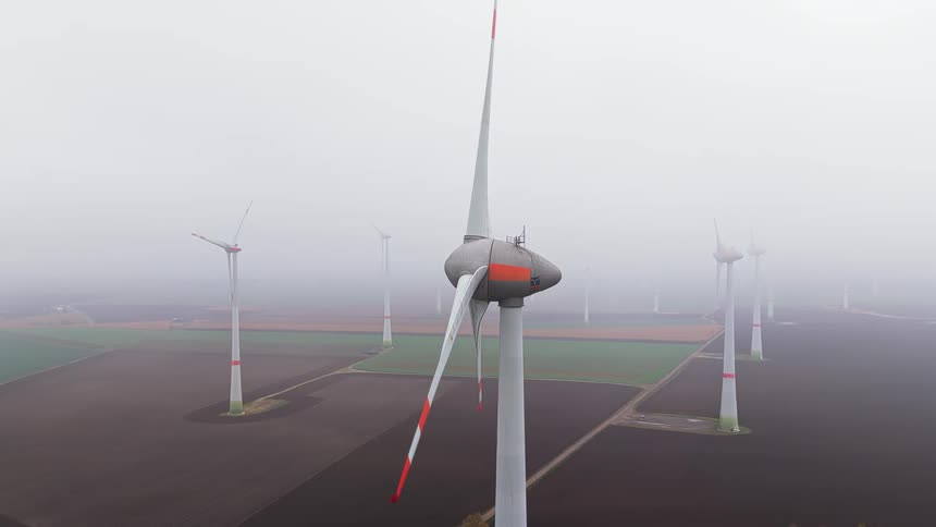 Wind turbines on a wind farm in a field covered in fog outdoors during day time