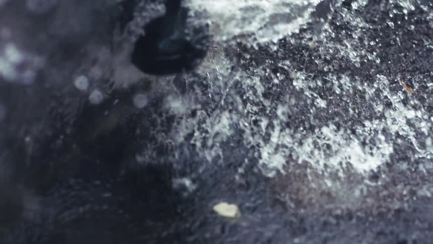 A close up of water splashing and falling onto a black shoe