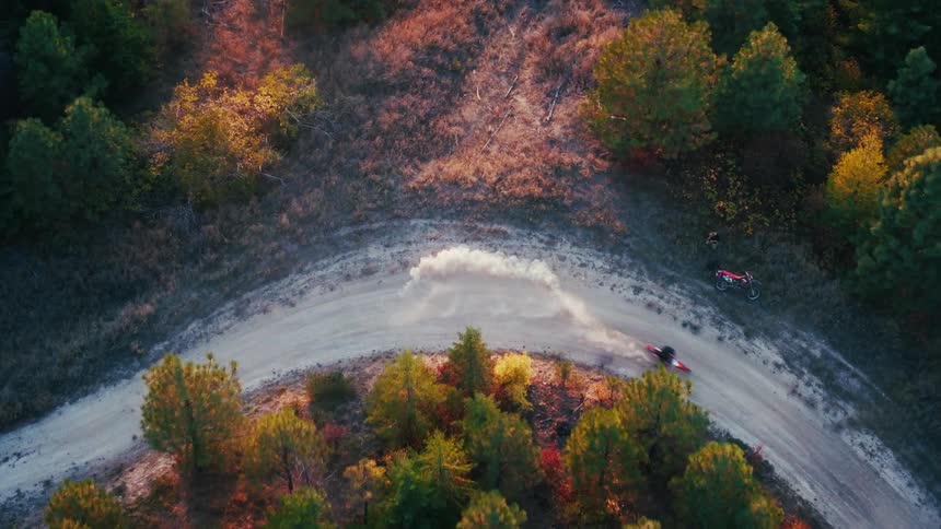Aerial view of a dirt road curve with a motorcyclist kicking up dust among trees