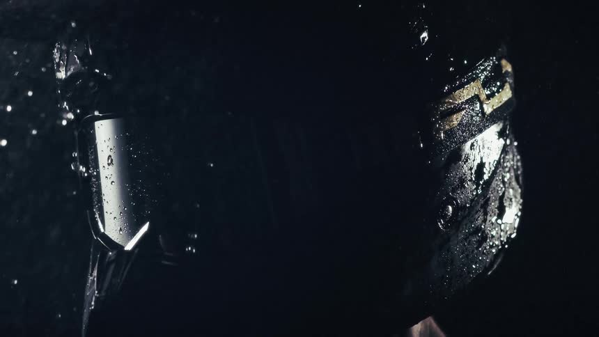 Water cascades over the helmet and goggles of a motocross driver in an intense slowmotion closeup each droplet glistening as it cuts through the darkness