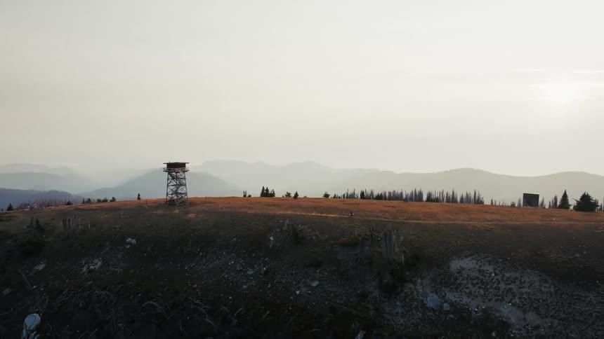 Hill with an observation tower surrounded by sparse vegetation and mountain ranges in the background