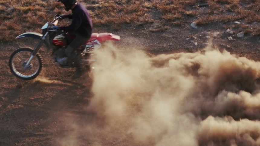 Motorcyclist turns quickly on a dirt road creating a cloud of dust during the daytime