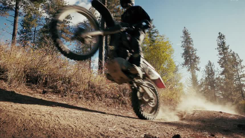 A man on a motorcycle pops a wheelie as he rides on a dirt path
