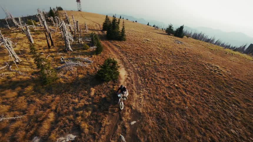Tracking a dirt bike rider across a rugged mountain ridge the camera performs a rapid dizzying spiral maneuver that spins the view to reveal a solitary fire lookout tower perched on the peak