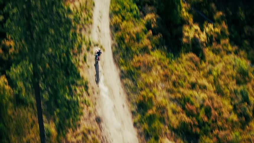 From a dizzying topdown aerial view a lone motocross rider speeds along a winding dirt trail the landscape blurring past in a rush of color and motion
