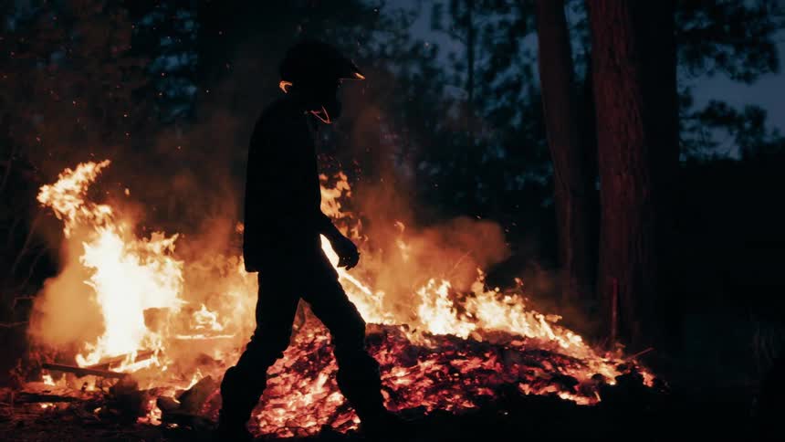 The man walks past a pile of burning leaves at night