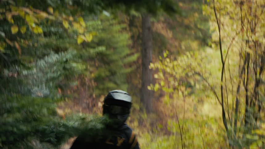 Motocross rider moving along a narrow trail in a forested area with dense foliage in the foreground