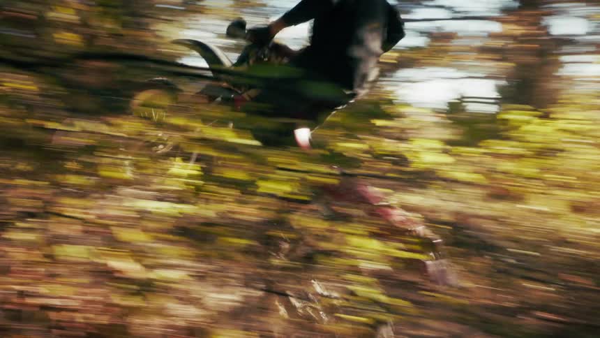 The man jumps over a hill on his dirt bike in the forest