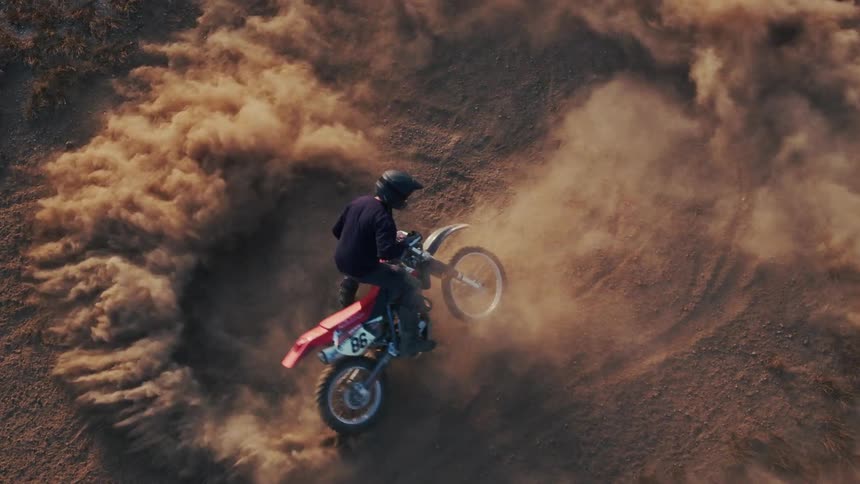 A motorcyclist doing doughnuts and kicking up a massive cloud of dust on a hillside