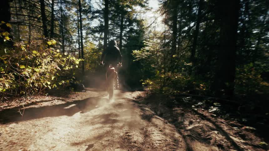 A man is standing as he rides his motorcycle through a forest