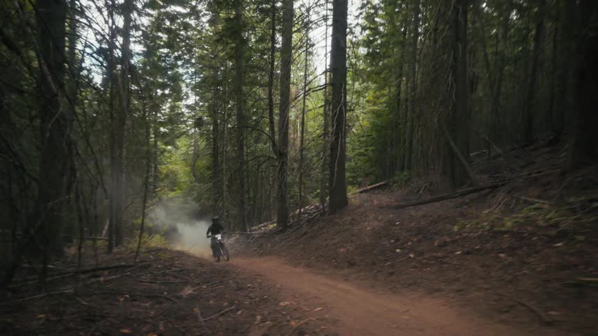 The man races his dirt bike on the small trail in the forest