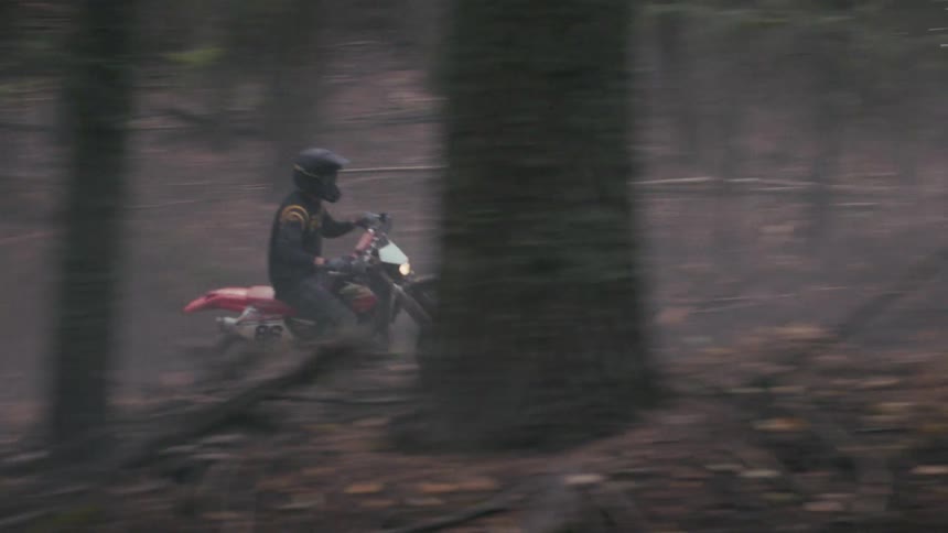 Biker wearing a helmet riding a motorcycle on a trail in the woods outdoors during day time