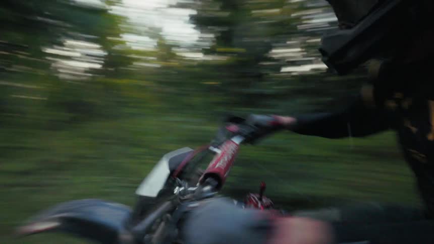 A motorcyclist rides a motorcycle down a dirt path through a lush forest