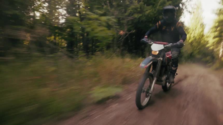 Motocross rider moving along a dirt trail in a forested area with motion blur